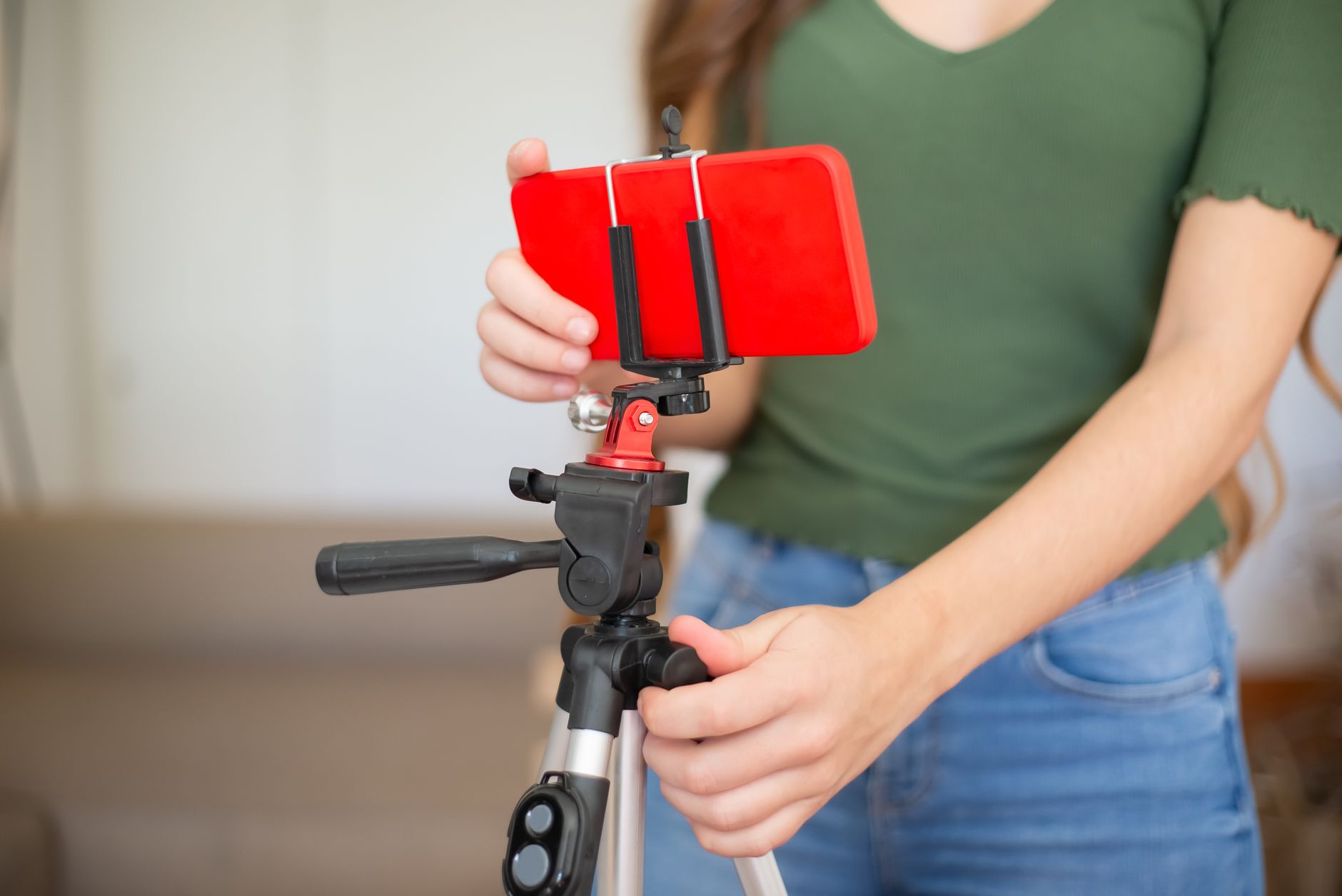 Une personne règle un smartphone rouge fixé sur un trépied, dans un salon, avant de filmer une vidéo